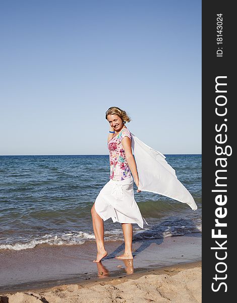 Beautiful girl standing with waving a scarf on the beach