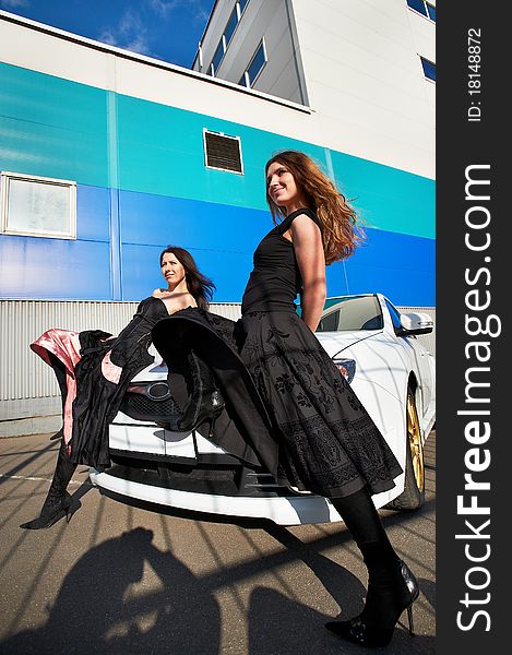 Two beautiful young woman and stylish white sports car on the background industrial building. Two beautiful young woman and stylish white sports car on the background industrial building