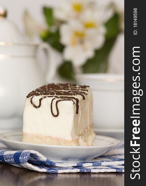 Dessert with icing and teapot on table against vase with flowers