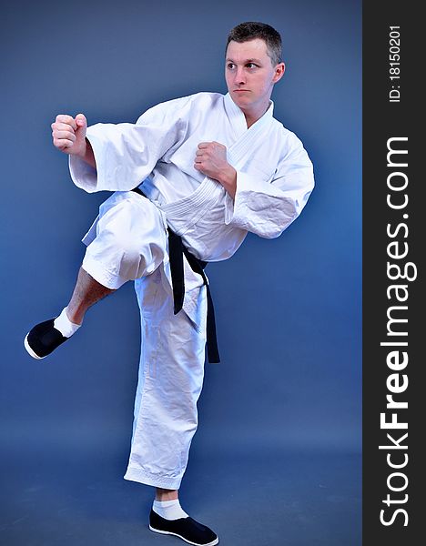 Young sporty karate man doing special exercise on gray background