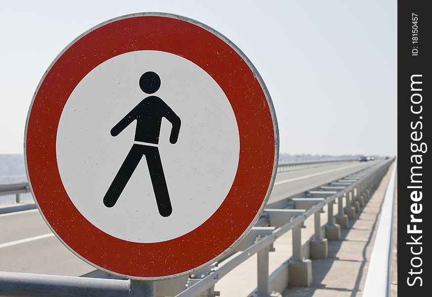 A damaged No trespassing sign at the side of the motorway. Defocused cars approaching.