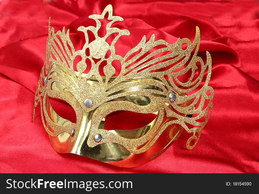 Gold mask with glitter on a satin red background. Gold mask with glitter on a satin red background