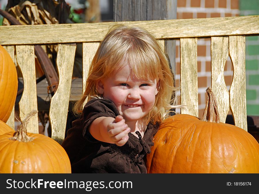 A cute, happy young girl sitting on a bench between some big pumpkins. A cute, happy young girl sitting on a bench between some big pumpkins.