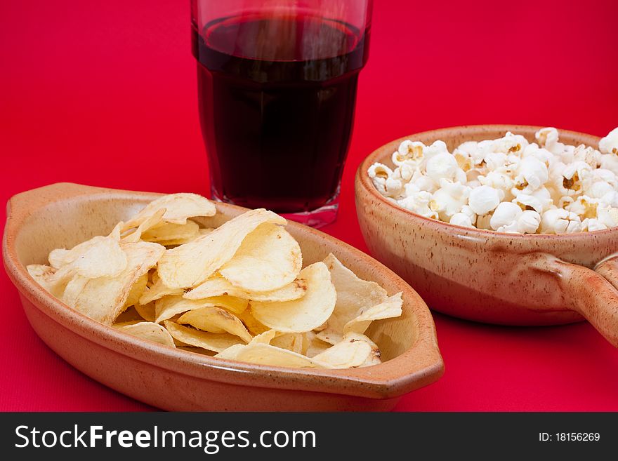 Tomato chips, pop corn and cola on red background