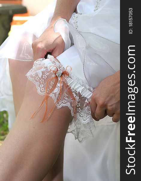 Bride in white wedding dress putting on her white and orange garter belt. Bride in white wedding dress putting on her white and orange garter belt