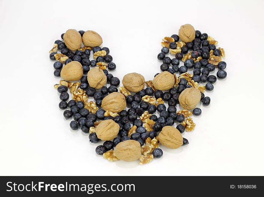 Whole fruit berry and unshelled and shelled nuts outline a shape of love on reflective white. Whole fruit berry and unshelled and shelled nuts outline a shape of love on reflective white.