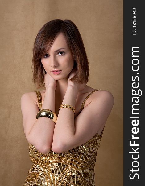 A portrait of a lovely young woman wearing a gold dress and gold bracelets against a gold background. A portrait of a lovely young woman wearing a gold dress and gold bracelets against a gold background