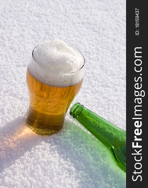 Beer in glass and green bottle on snow