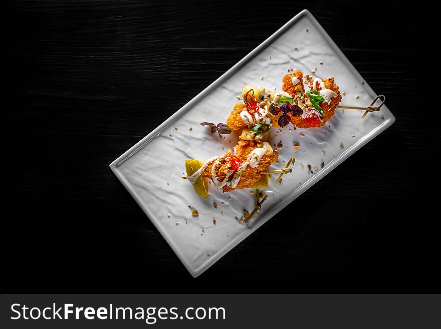 Spicy fried shrimp skewers served on plate on black wooden table background