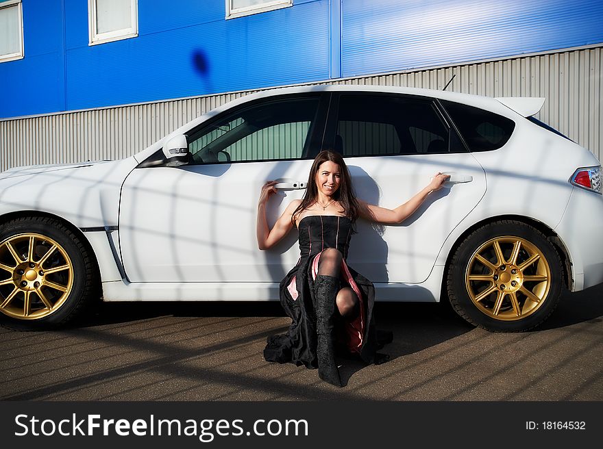 Young woman near white sports car on background industrial building