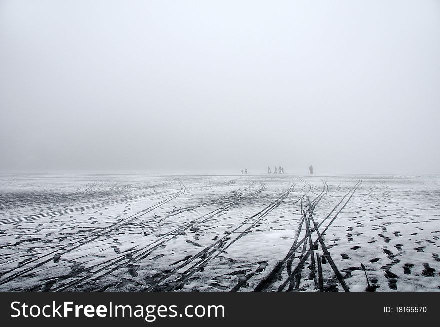 A distant cluster of people walking on melting ice on a lake in a dence winter fog. A distant cluster of people walking on melting ice on a lake in a dence winter fog