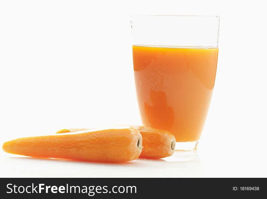 Two carrots close to a glass of fresh carrot juice