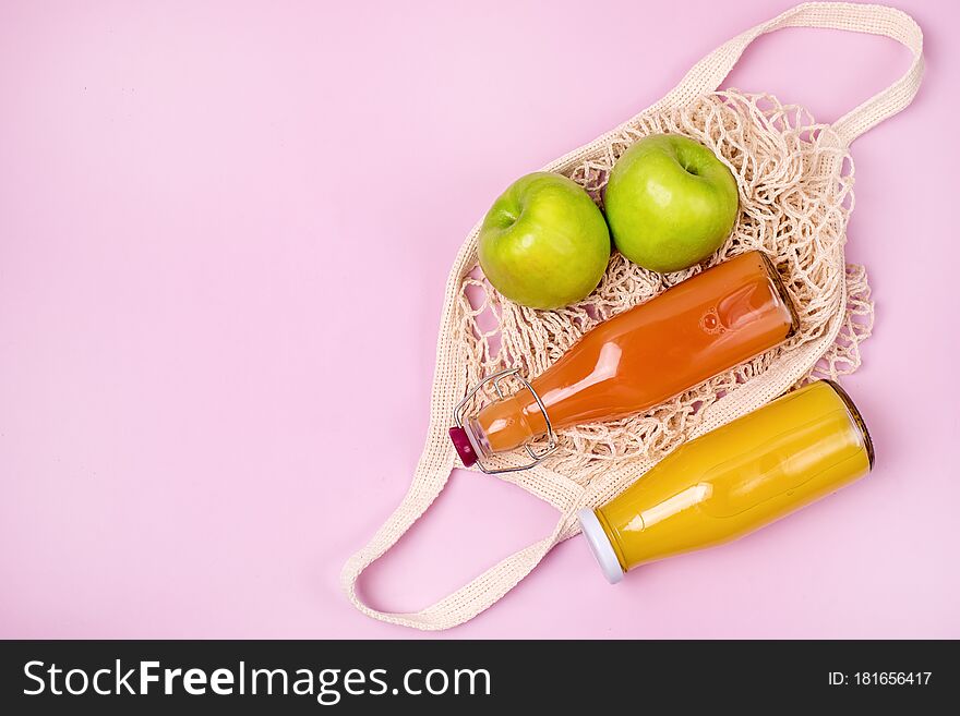 Bag with Two Bottles of Citrus Juice Green Apples Diet Food Top View Horizontal Pink Background.