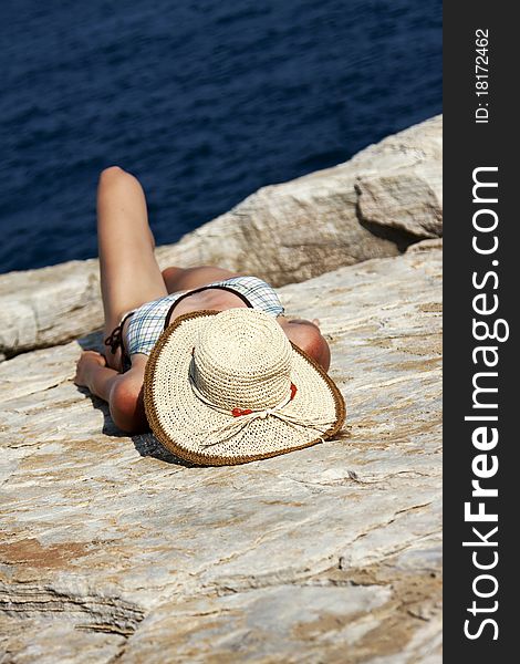 Woman with hat sunbathing on rocks