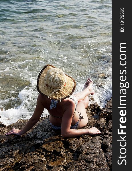 Woman with hat sunbathing on rocks