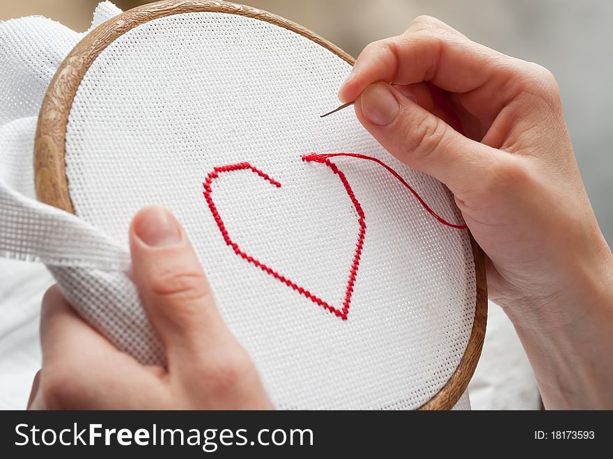 Female hands embroidering red heart. Female hands embroidering red heart