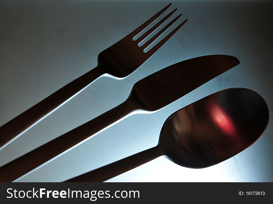 Close-up of eating set (knife, fork and spoon) in smooth red light against grey background. Close-up of eating set (knife, fork and spoon) in smooth red light against grey background.