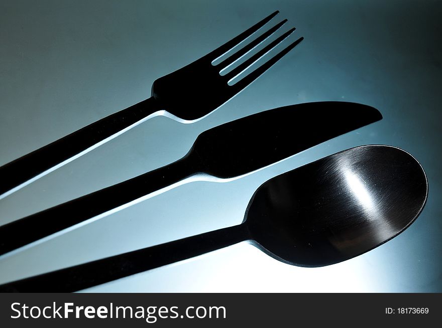 Close-up of eating set (knife, fork and spoon) in smooth white light against light blue background. Close-up of eating set (knife, fork and spoon) in smooth white light against light blue background.