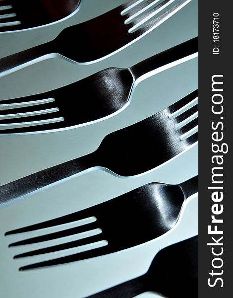 Close-up of six stainless steel eating forks in smooth white light against light blue background.