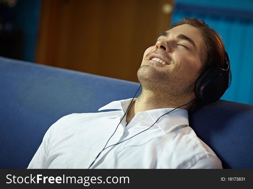 Caucasian adult man relaxing on sofa with headphones. Horizontal shape, side view, head and shoulders, copy space. Caucasian adult man relaxing on sofa with headphones. Horizontal shape, side view, head and shoulders, copy space