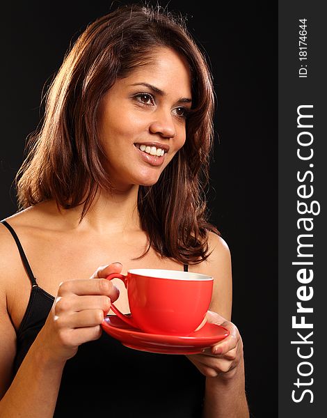 Portrait of a beautiful smiling young ethnic woman holding a cup of tea. Woman is wearing a black vest and the cup and saucer are both red. Portrait of a beautiful smiling young ethnic woman holding a cup of tea. Woman is wearing a black vest and the cup and saucer are both red.