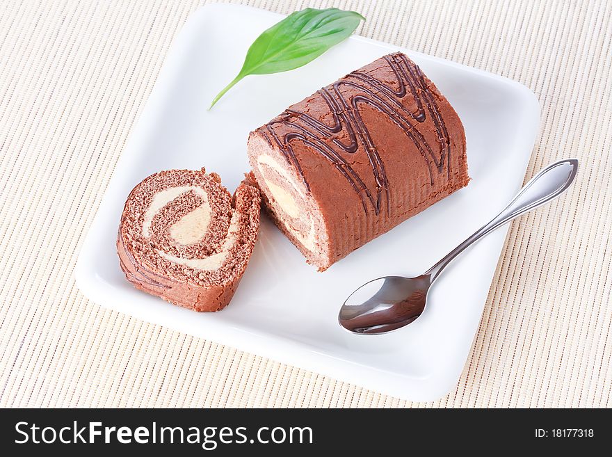 Closeup swiss roll with condensed milk cream on white plate with spoon and a green leaf. Closeup swiss roll with condensed milk cream on white plate with spoon and a green leaf