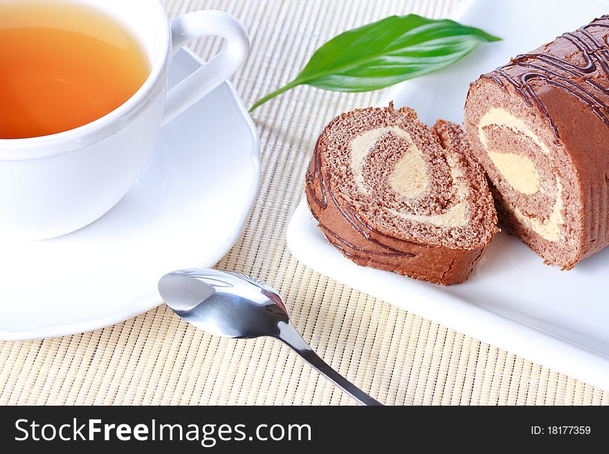 Closeup swiss roll with condensed milk cream on white plate and a cup of tea. Closeup swiss roll with condensed milk cream on white plate and a cup of tea