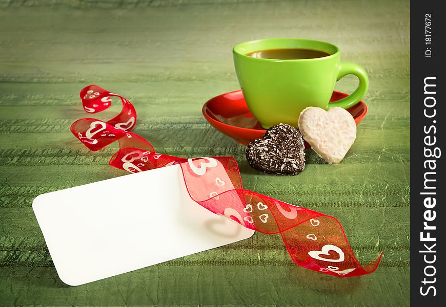 Green background with cup of tea, cookies empty card and red ribbon