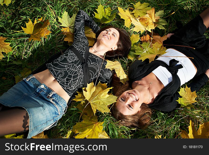 Two happy young woman on green grass and yellow leaves in park. Two happy young woman on green grass and yellow leaves in park