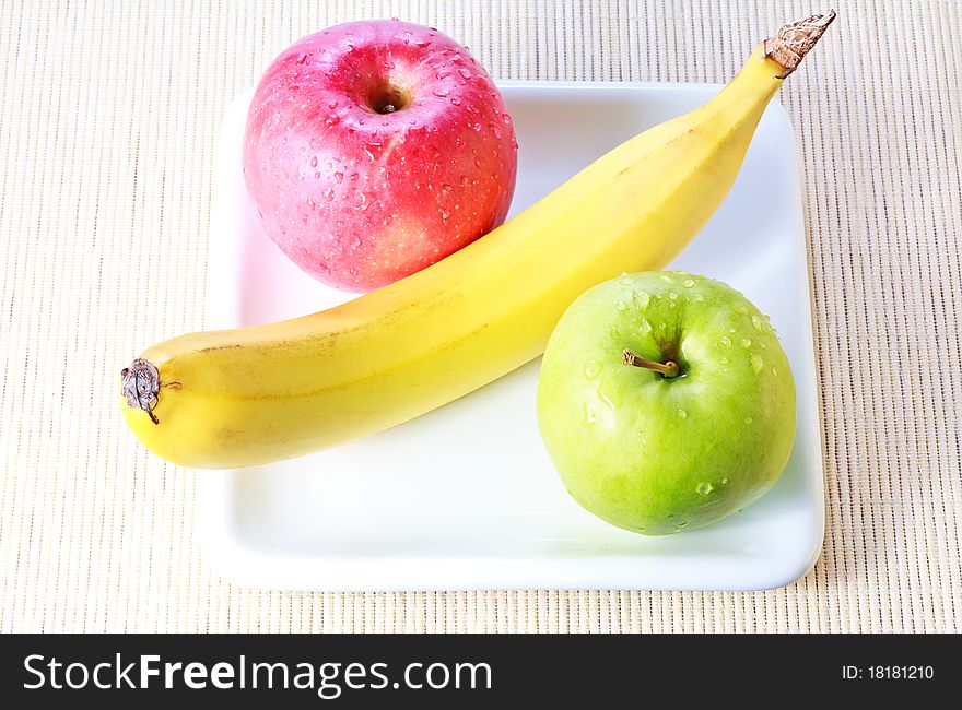 Banana, green and red apples on plate