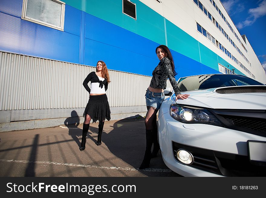 Two beautiful girls friend and stylish white sports car on the background industrial building. Two beautiful girls friend and stylish white sports car on the background industrial building