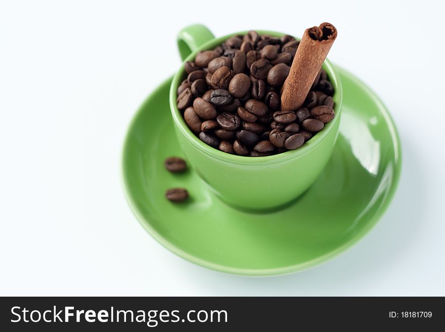 Aromatic roasted coffee beans with cinnamon sticks stand in the green cup. Aromatic roasted coffee beans with cinnamon sticks stand in the green cup