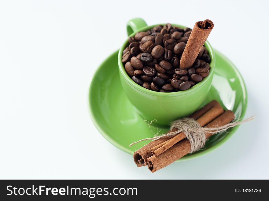 Aromatic roasted coffee beans with cinnamon sticks stand in the green cup. Aromatic roasted coffee beans with cinnamon sticks stand in the green cup