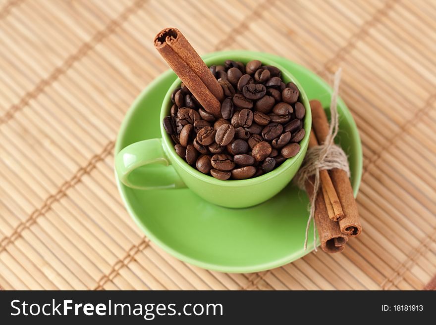 Coffee beans and cinnamon stick in a green cup on wooden surfaces