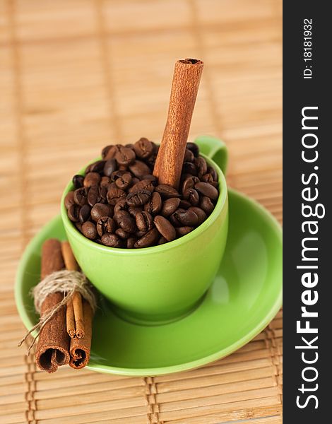 Coffee beans and cinnamon stick in a green cup