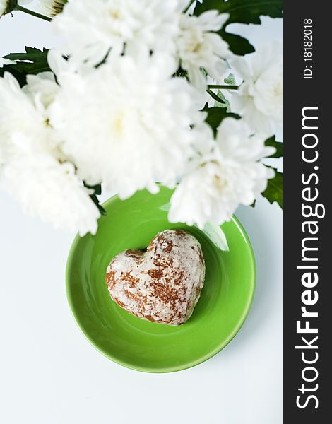 Cookies in a heart on a green plate near a bouquet of white flowers. Cookies in a heart on a green plate near a bouquet of white flowers