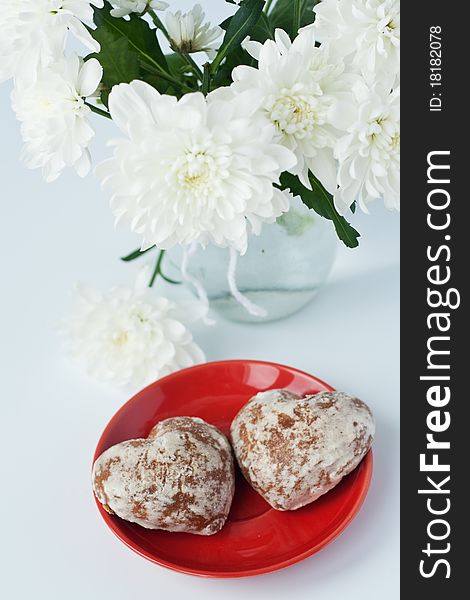 Cookies in a heart on a red plate near a bouquet of white flowers. Cookies in a heart on a red plate near a bouquet of white flowers