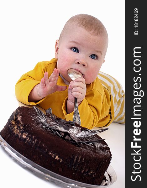 The baby with a big spoon in hand wants to eat chocolate cake