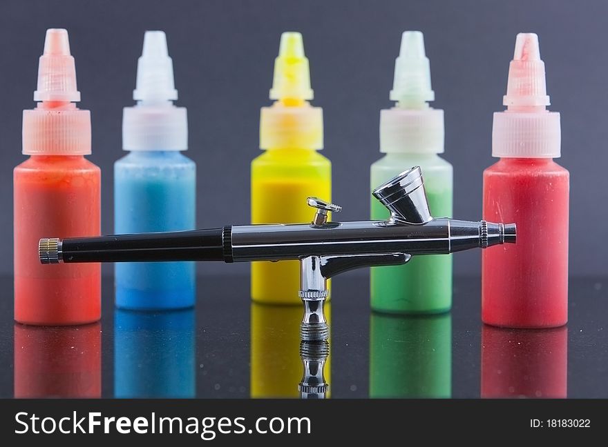 A silver airbrush against a background of out of focus and blurred bottles of spray paint. A silver airbrush against a background of out of focus and blurred bottles of spray paint