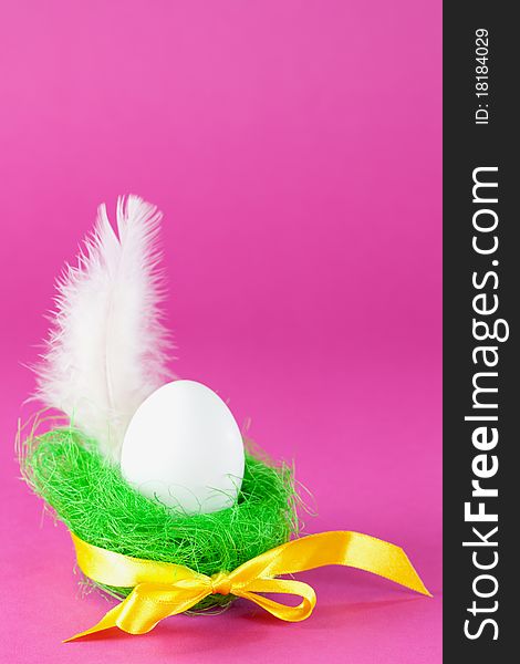 Easter egg in green basket with feather and ribbon in front of pink background with copy space. Easter egg in green basket with feather and ribbon in front of pink background with copy space