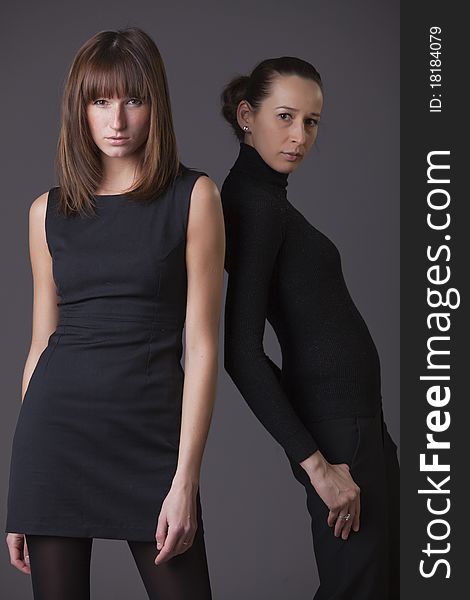 Two fashion female models posing in studio over grey background. Two fashion female models posing in studio over grey background