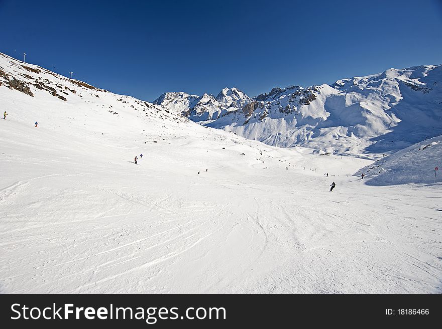 View down a piste with skiers and mountains. View down a piste with skiers and mountains