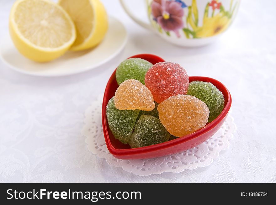 Colorful sweets in a heart-shape vase in a tea table, close up. Colorful sweets in a heart-shape vase in a tea table, close up