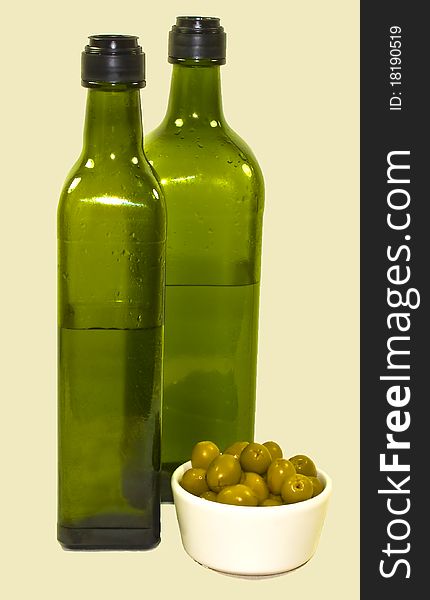 A close up of two green olive oil bottles and a bowl of green olives. A close up of two green olive oil bottles and a bowl of green olives