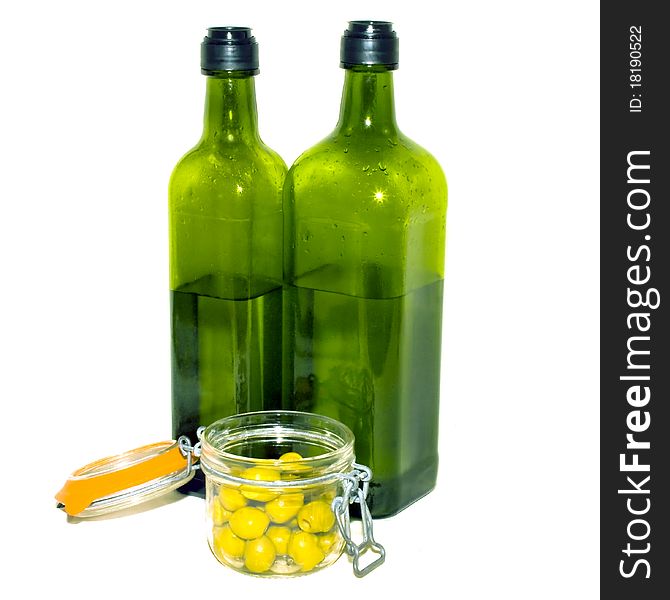 A close up of two green bottles of olive oil and a jar of green olives. A close up of two green bottles of olive oil and a jar of green olives