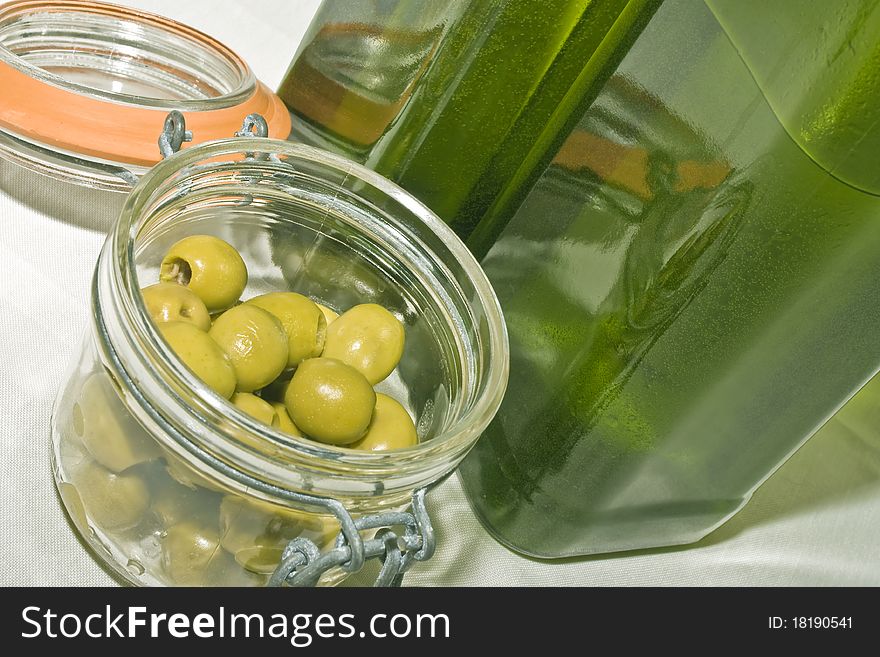 A close up of two greenolive oil bottles and a jar of green olives. A close up of two greenolive oil bottles and a jar of green olives