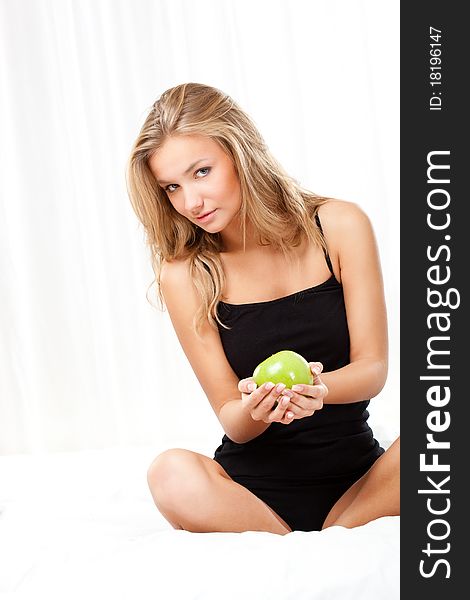 Beautiful blonde woman sitting on bed and holding apple