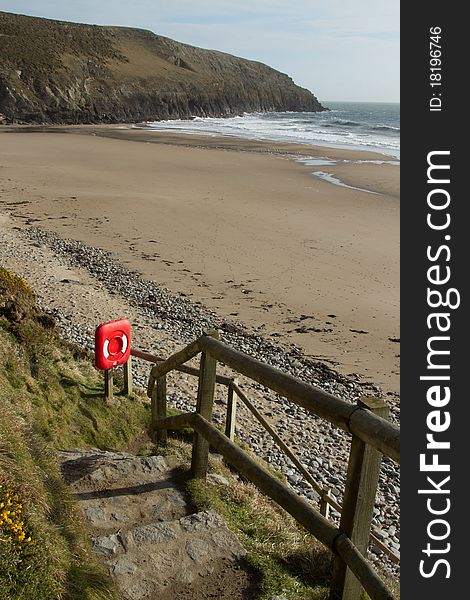 Stone step public footpath with hand rail containing life saving equipment box in red leads to a beach with sand sea and cliff. Stone step public footpath with hand rail containing life saving equipment box in red leads to a beach with sand sea and cliff.