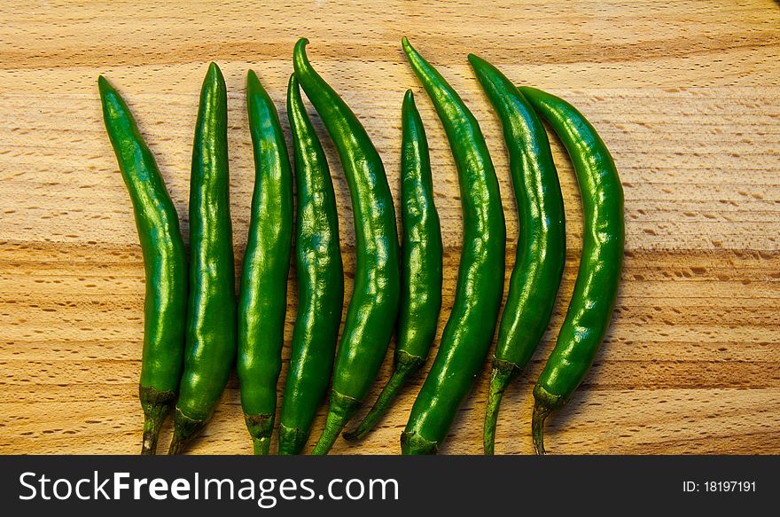 Green chilli peppers on a wooden chopping board.