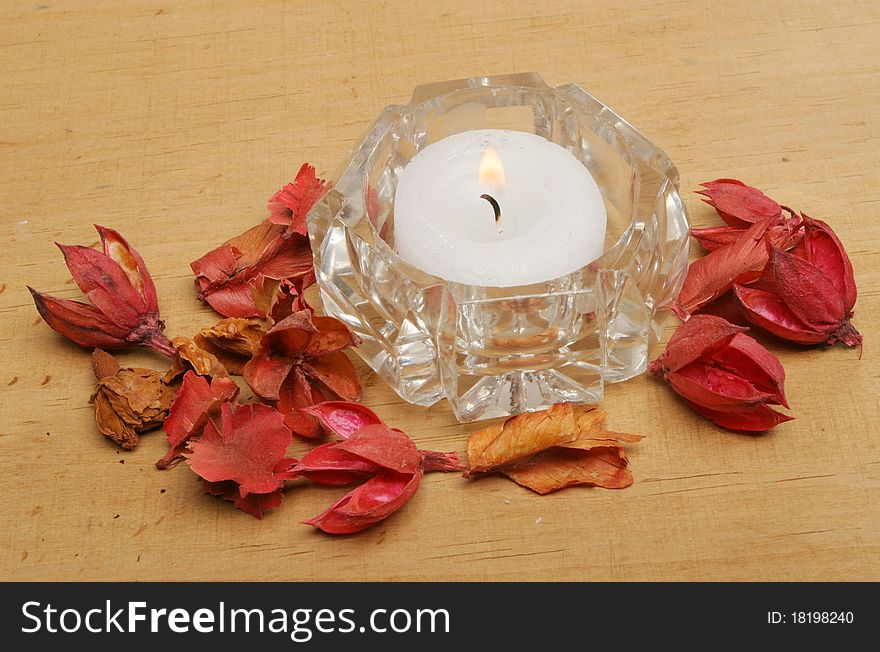 Tea light candle in a crystal glass holder with potpourri on a wooden board